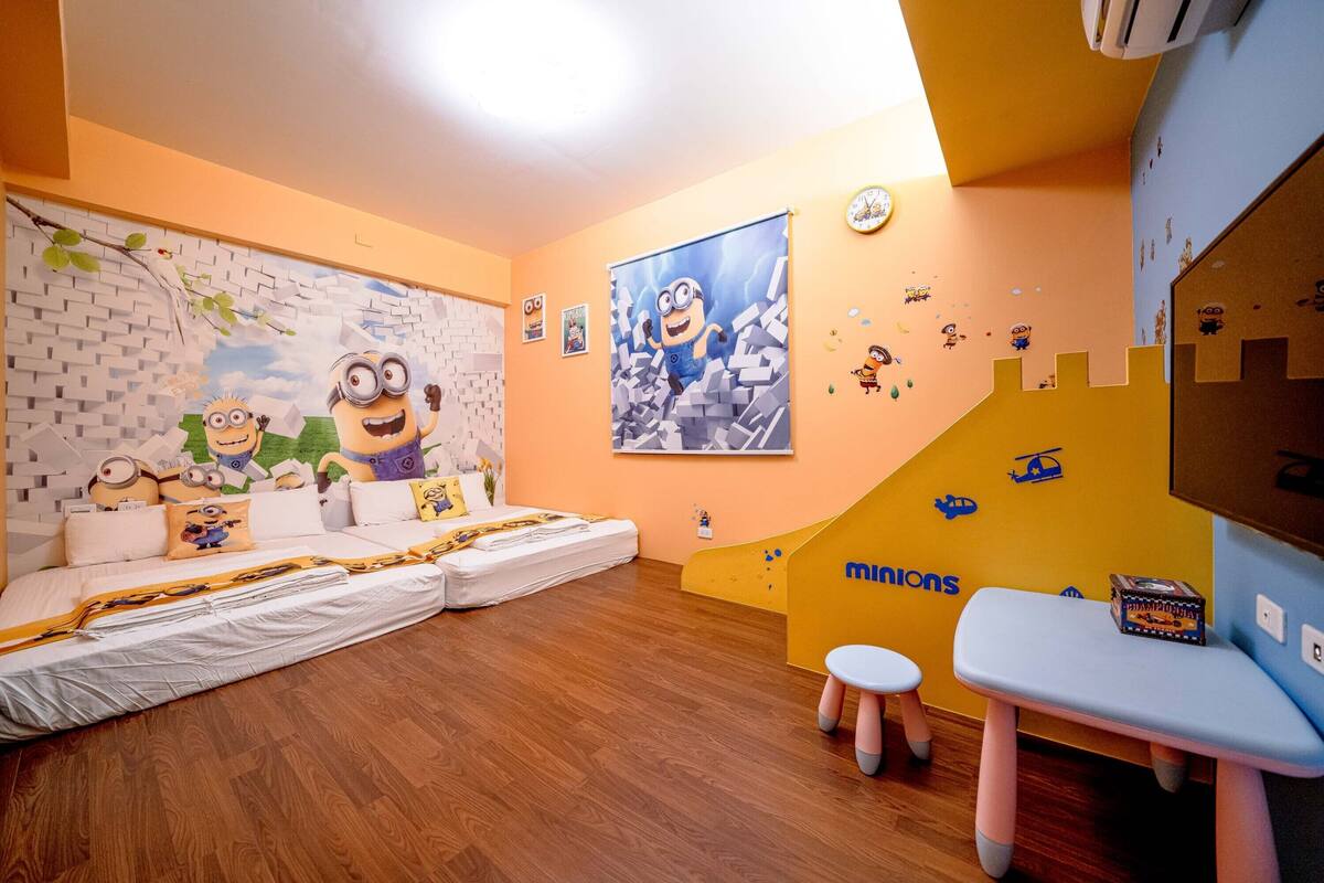 A room with a Minions-themed wall mural, a sofa, a small table, and a play area with a slide.