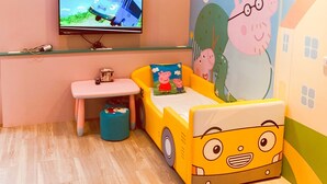 Une chambre d’enfant avec une télévision, un petit bureau, un lit en forme de bus et une fresque murale.