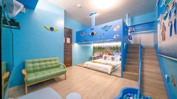 A children's room with a bunk bed, a green sofa, a play area with balls, and a wall decorated with car and space shuttle stickers.