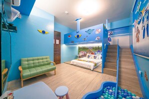 Ein Kinderzimmer mit Etagenbett, einem grünen Sofa, einem Spielbereich mit Bällen und einer Wand mit Aufklebern von Autos und Raumfähren.