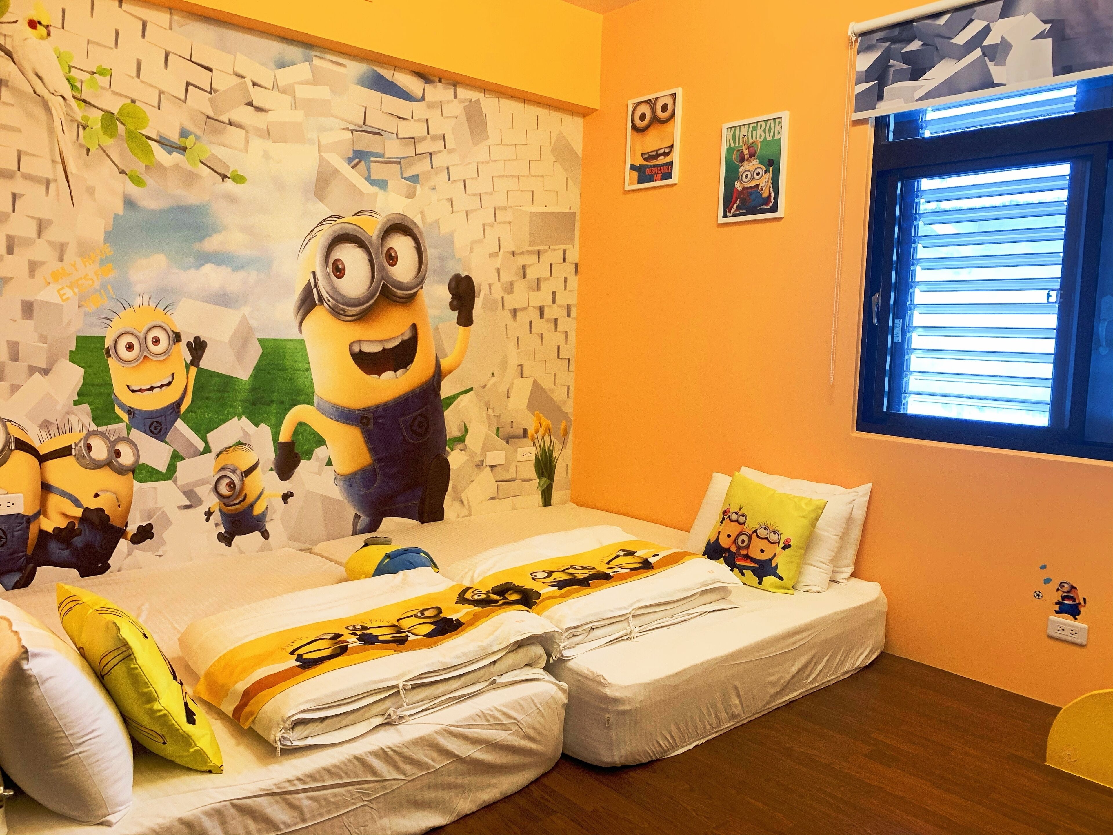 Een kindvriendelijke kamer met een Minion muurschildering, een bed met Minion beddengoed, en een raam met zonwering.
