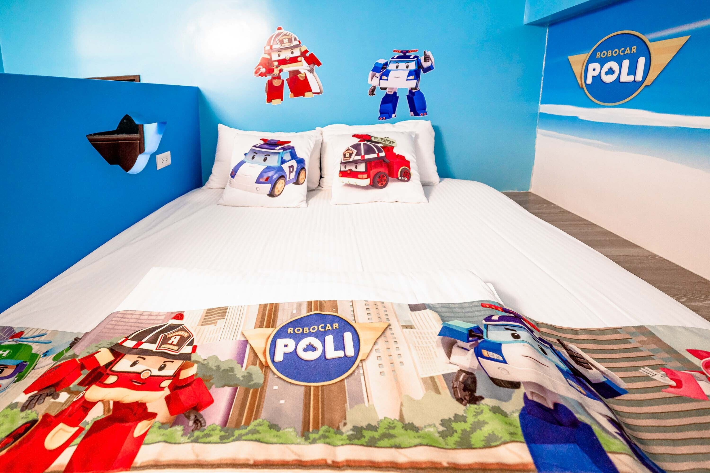 A children's room with blue walls, featuring a bed with white bedding and pillows with toy cars.