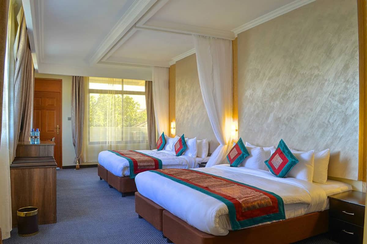 Een hotelkamer met twee bedden, een houten bureau en een groot raam met gordijnen.