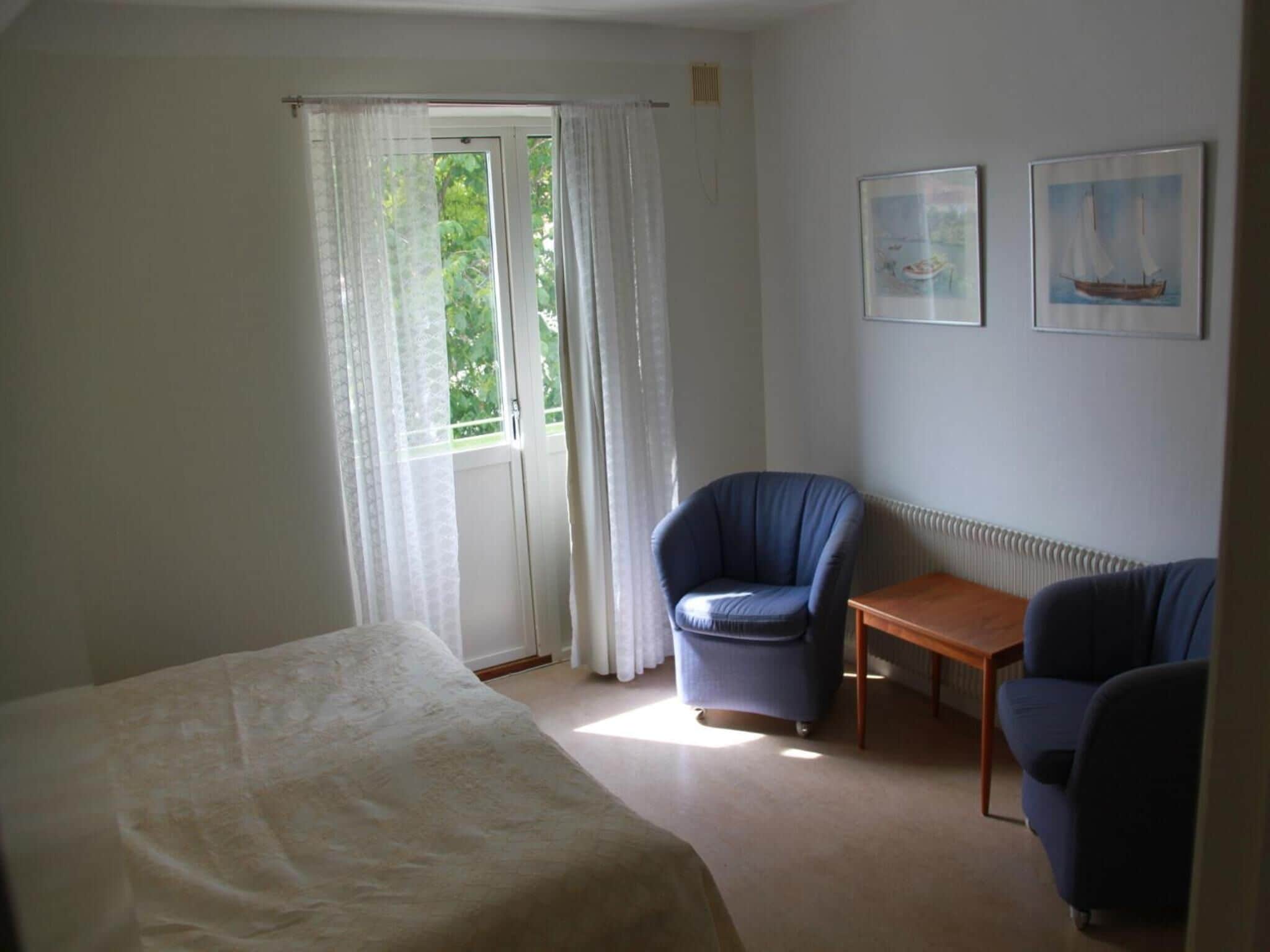 Un dormitorio con cama, dos sillas, una mesita y una ventana con cortinas.