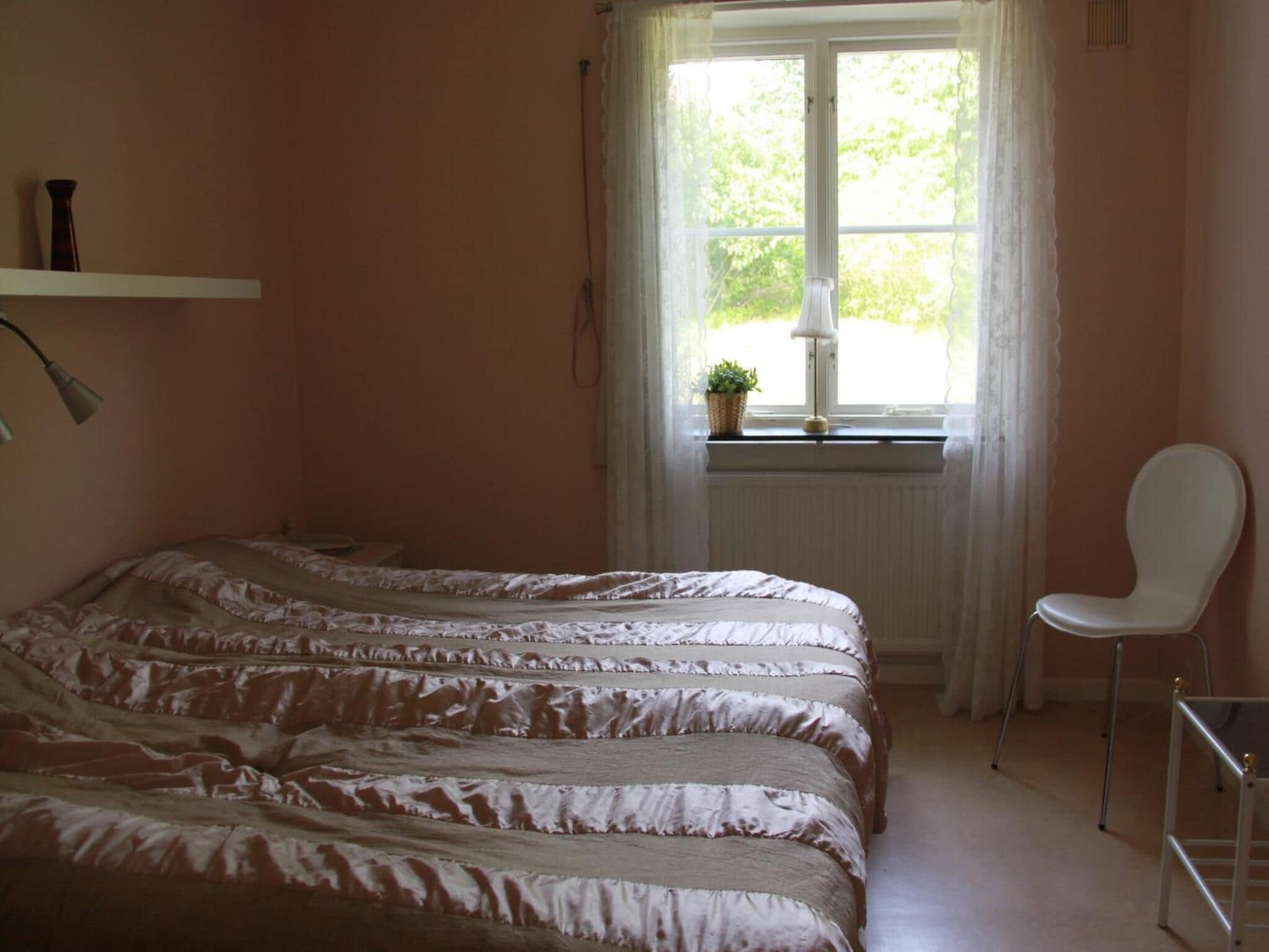 A bedroom with a bed, a chair, a window with curtains, and a shelf with items.