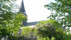A church with a steeple and clock, surrounded by greenery and a stone wall. - Fjällbacka Pensionat & Vandrarhem (Fjallbacka)