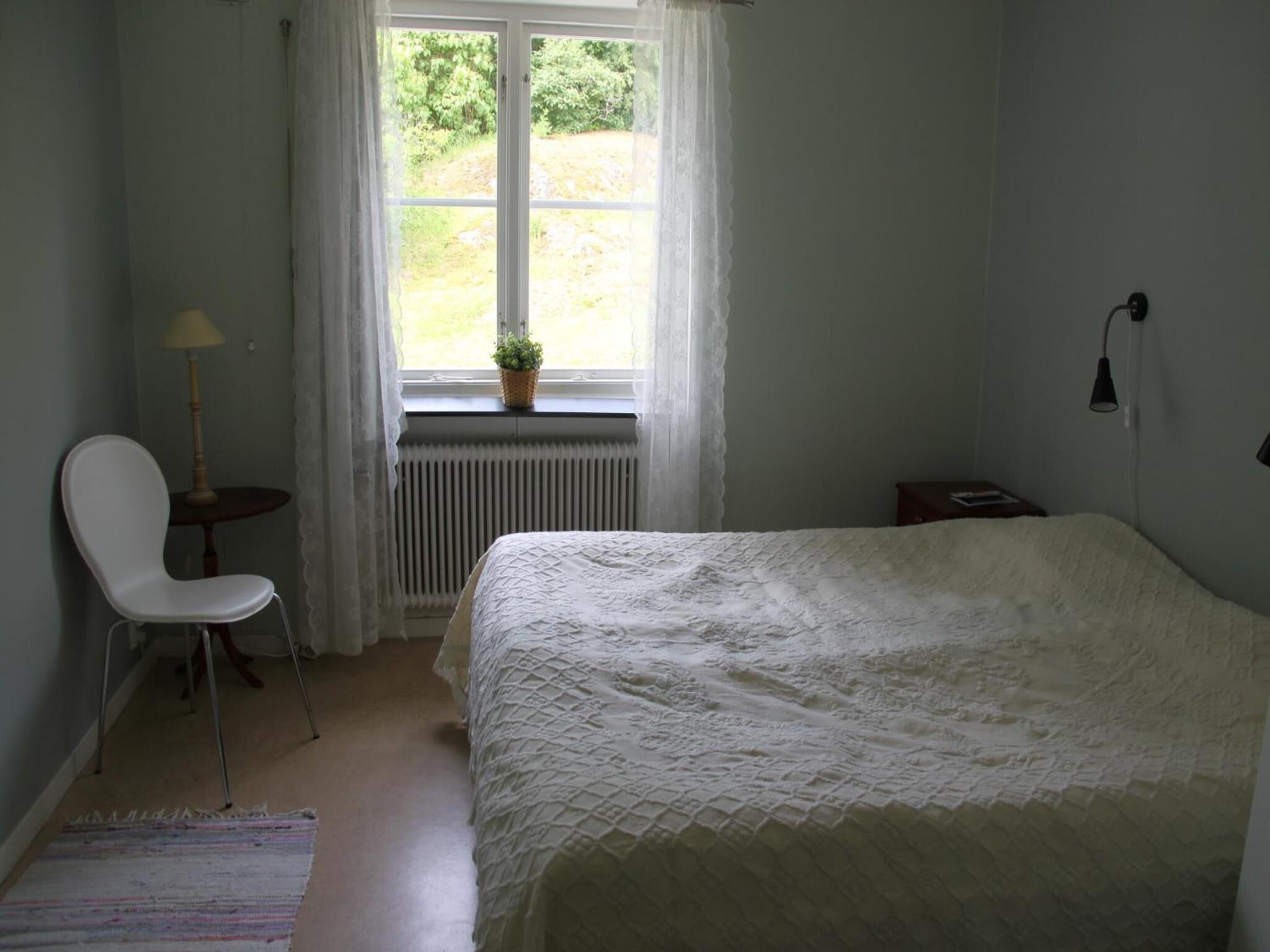Ein Schlafzimmer mit Bett, Sessel, einem kleinen Tisch, einem Fenster mit Blick auf Grünflächen und einer Heizung.