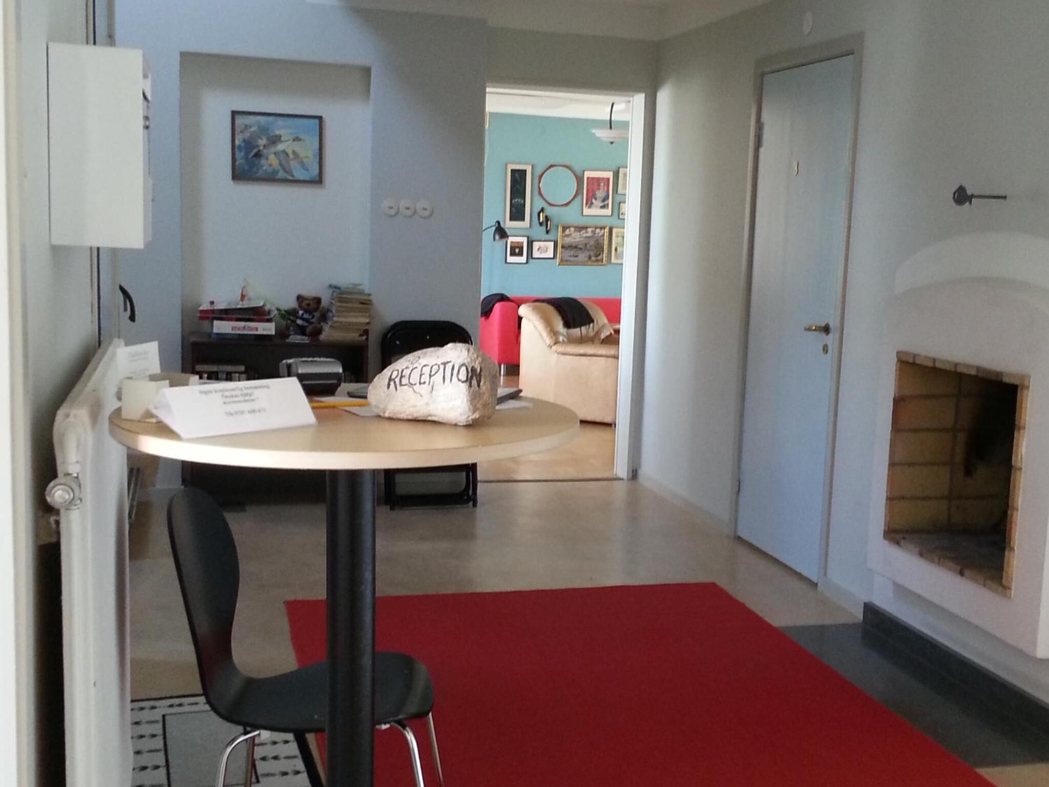 A reception area with a desk, a chair, a red carpet, a fireplace, and a wall with framed pictures.