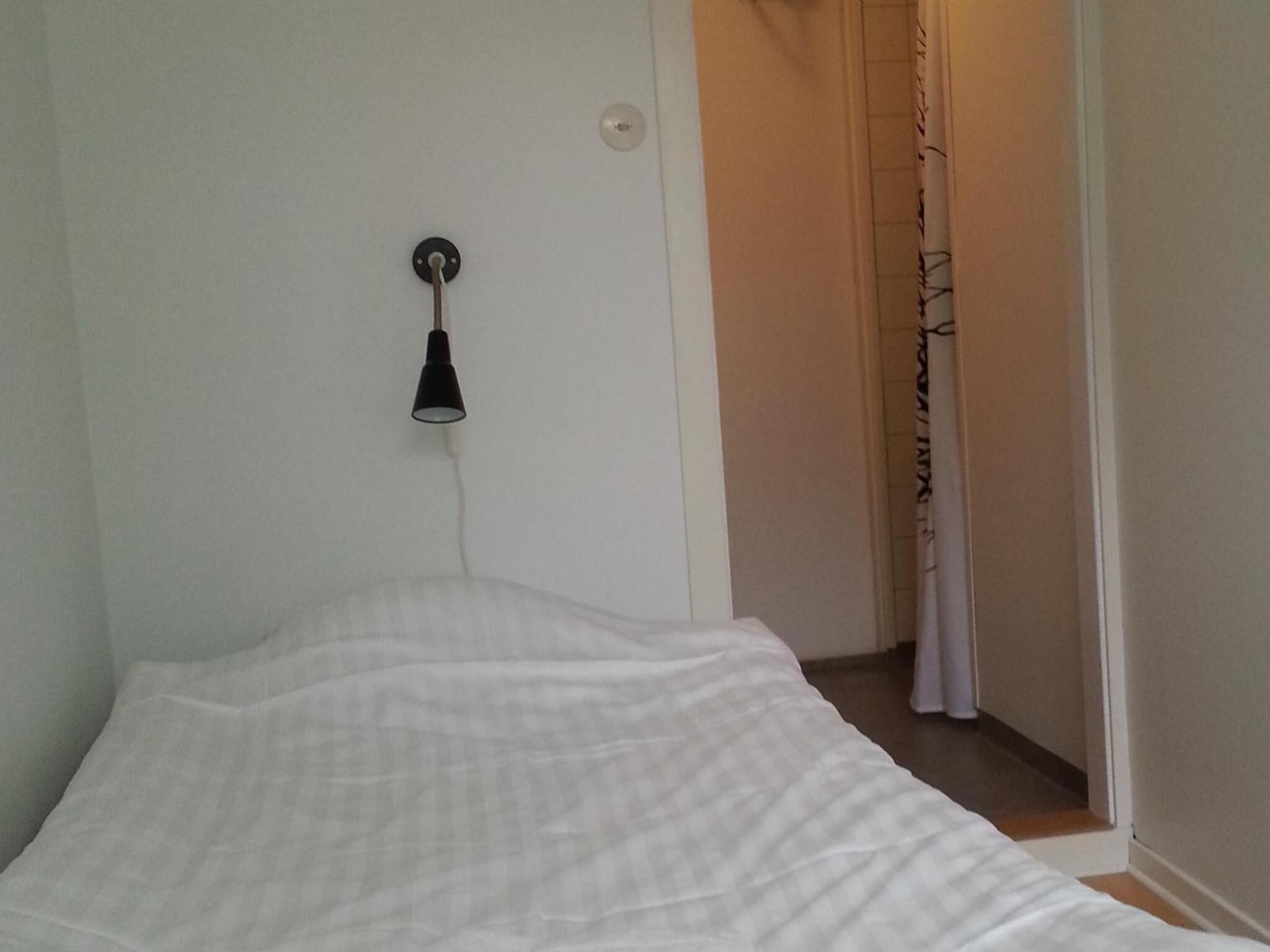 Et soveværelse med en seng, en lampe på væggen og en dør til et andet rum.