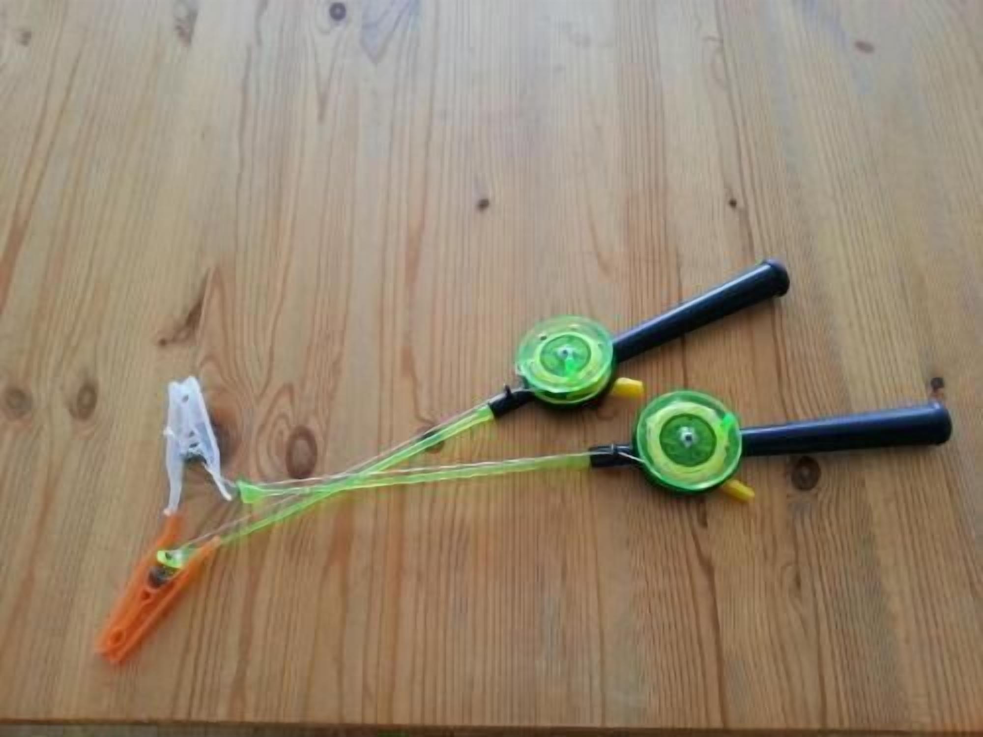 A wooden surface with two green and black objects with yellow handles and orange parts.