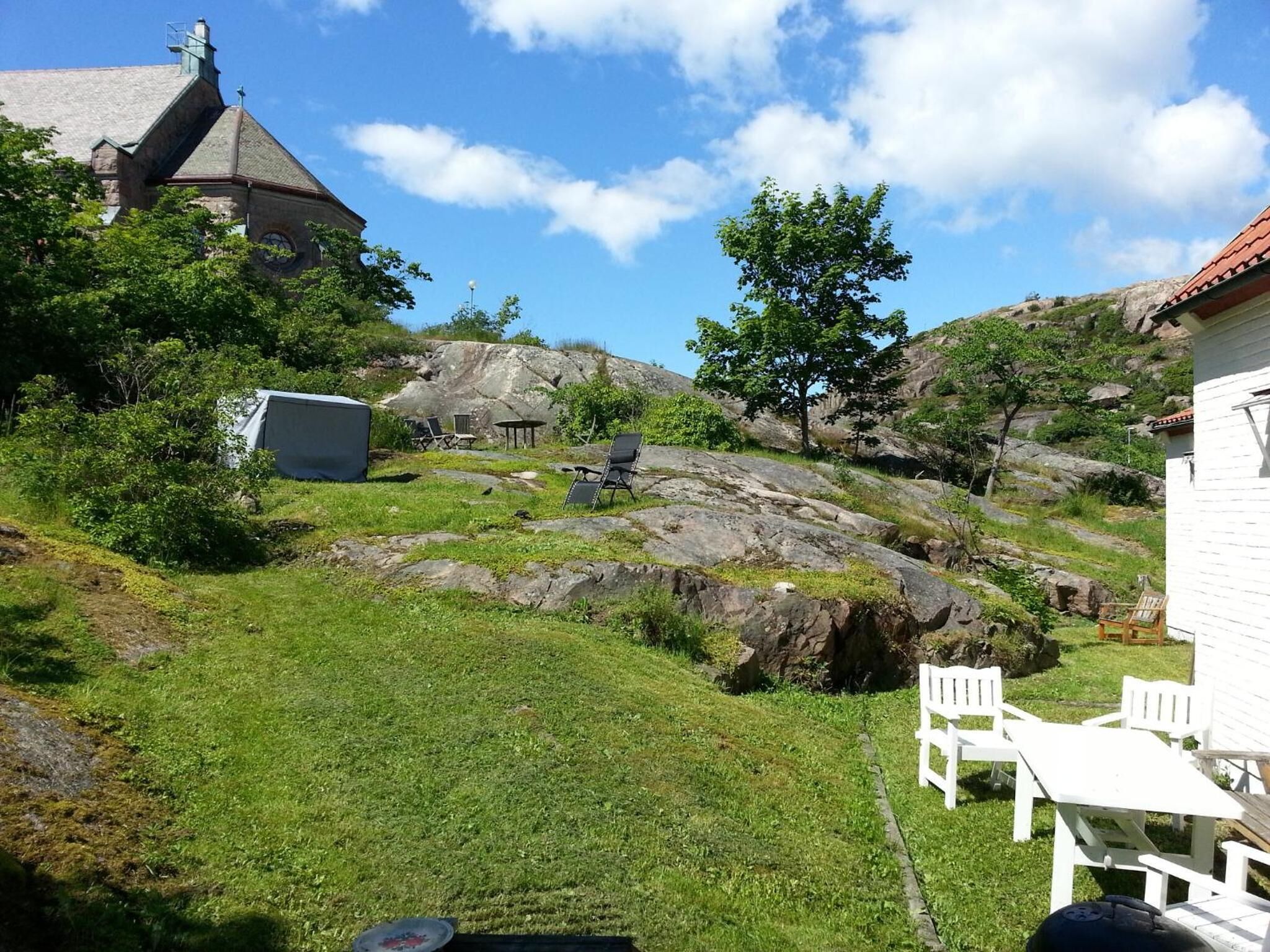 A grassy outdoor area with a white building, a stone structure, and a tree.
