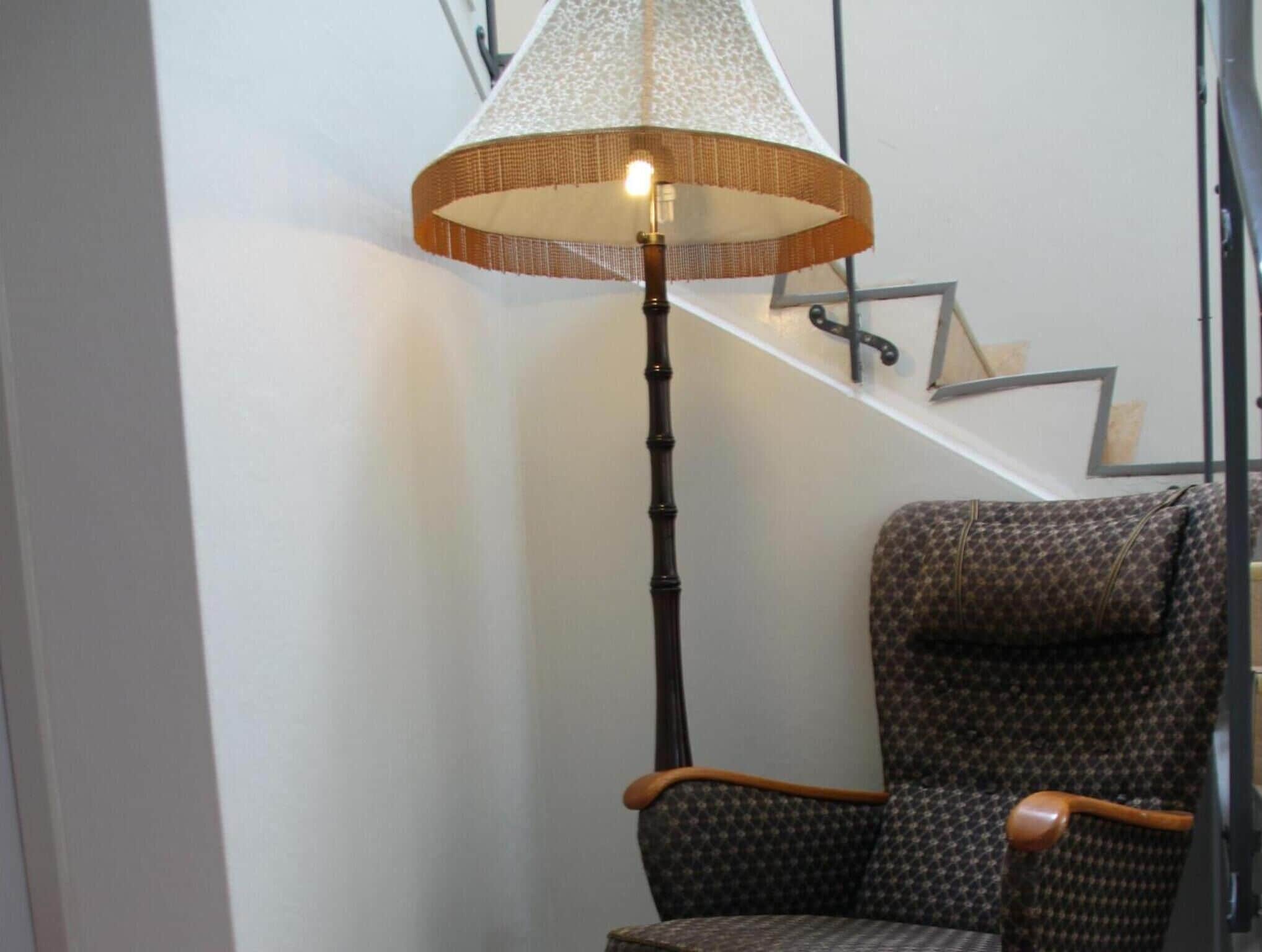 A corner of a room with a patterned chair, a tall floor lamp, and a staircase with a geometric design.