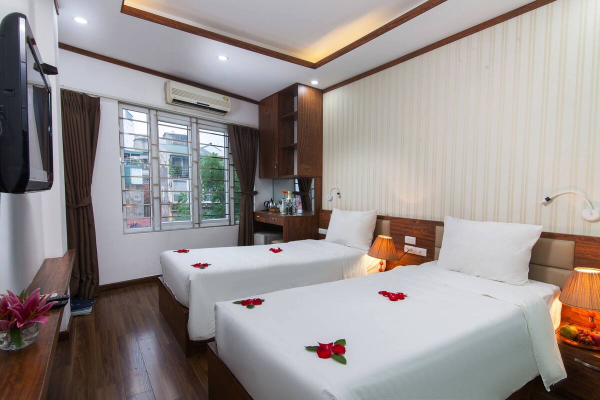 Une chambre d’hôtel avec deux lits, une télévision, un bureau et une fenêtre avec des rideaux.
