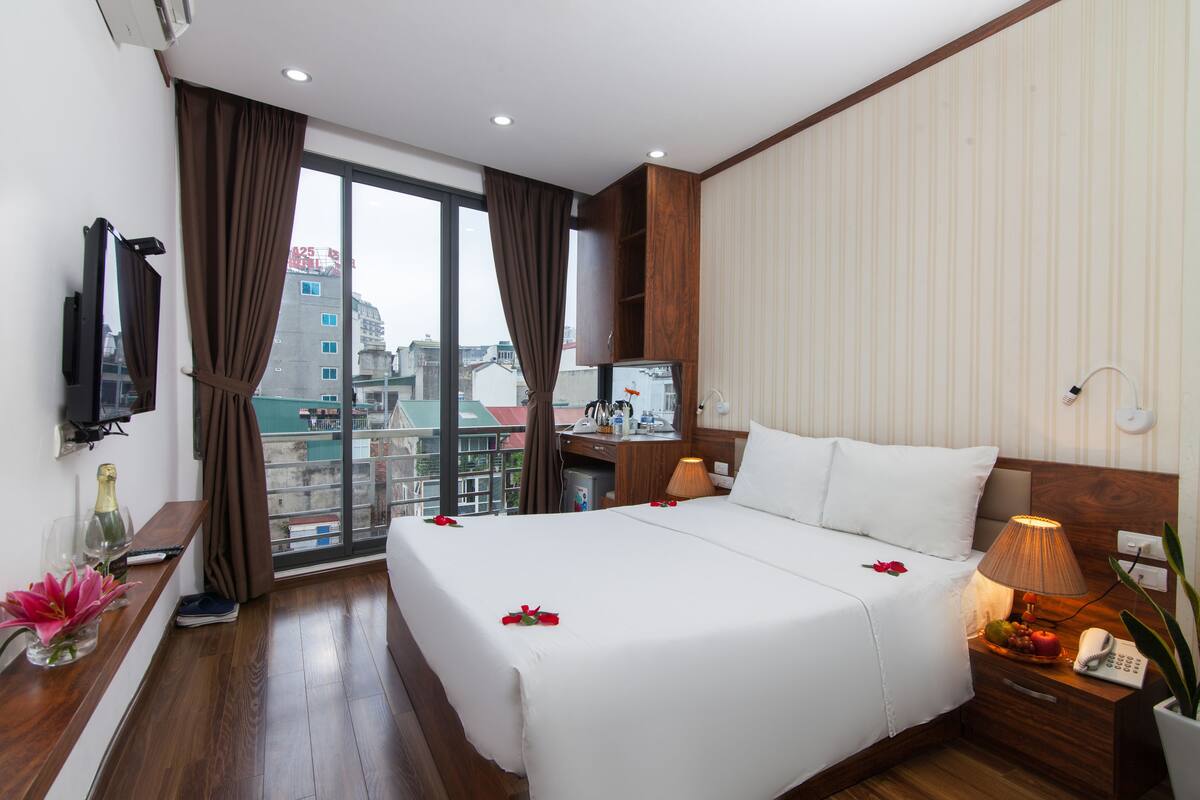 Une chambre d’hôtel avec un grand lit, un bureau, une chaise, une télévision et un balcon offrant une vue sur la ville.