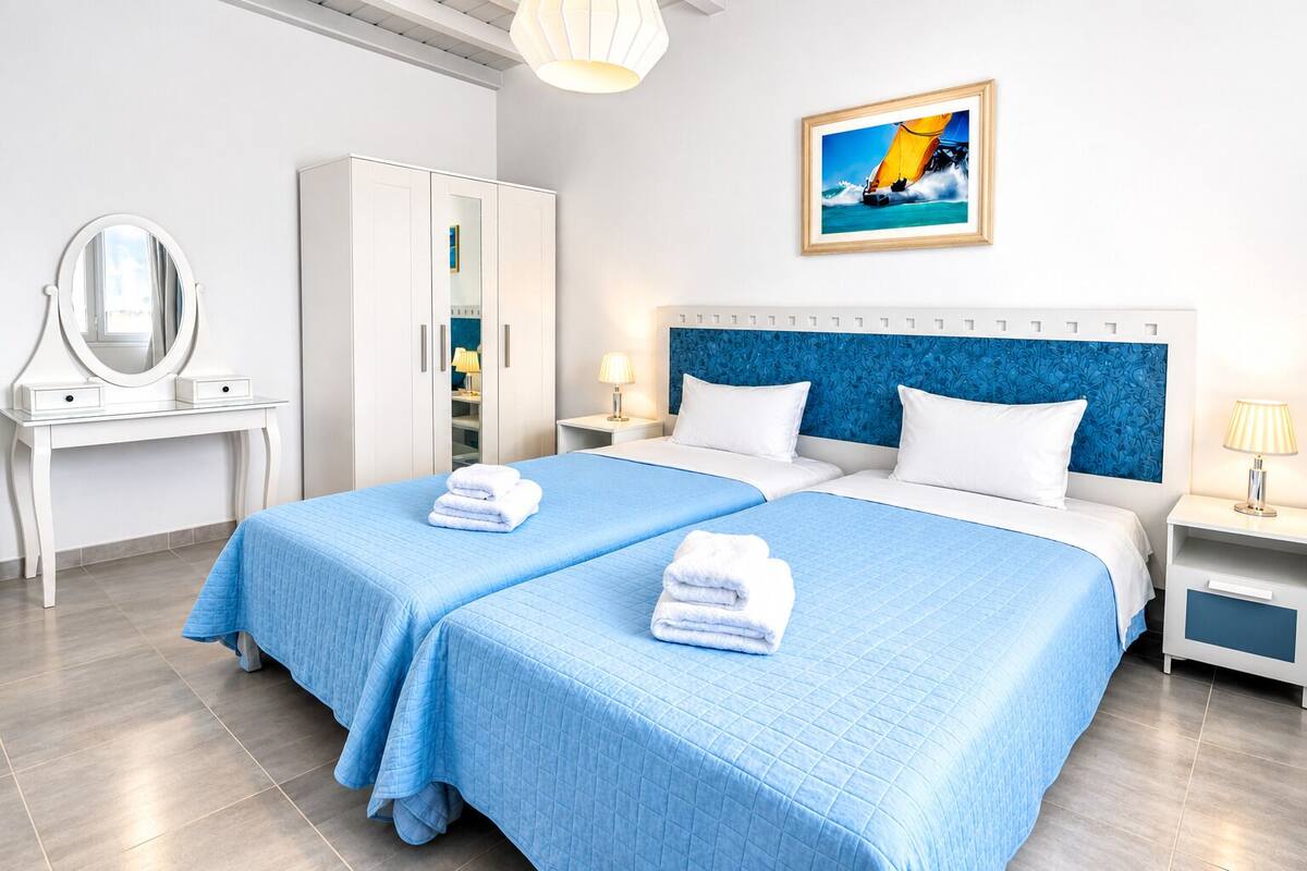 A hotel room with two beds, a wardrobe, a mirror, and a painting on the wall.