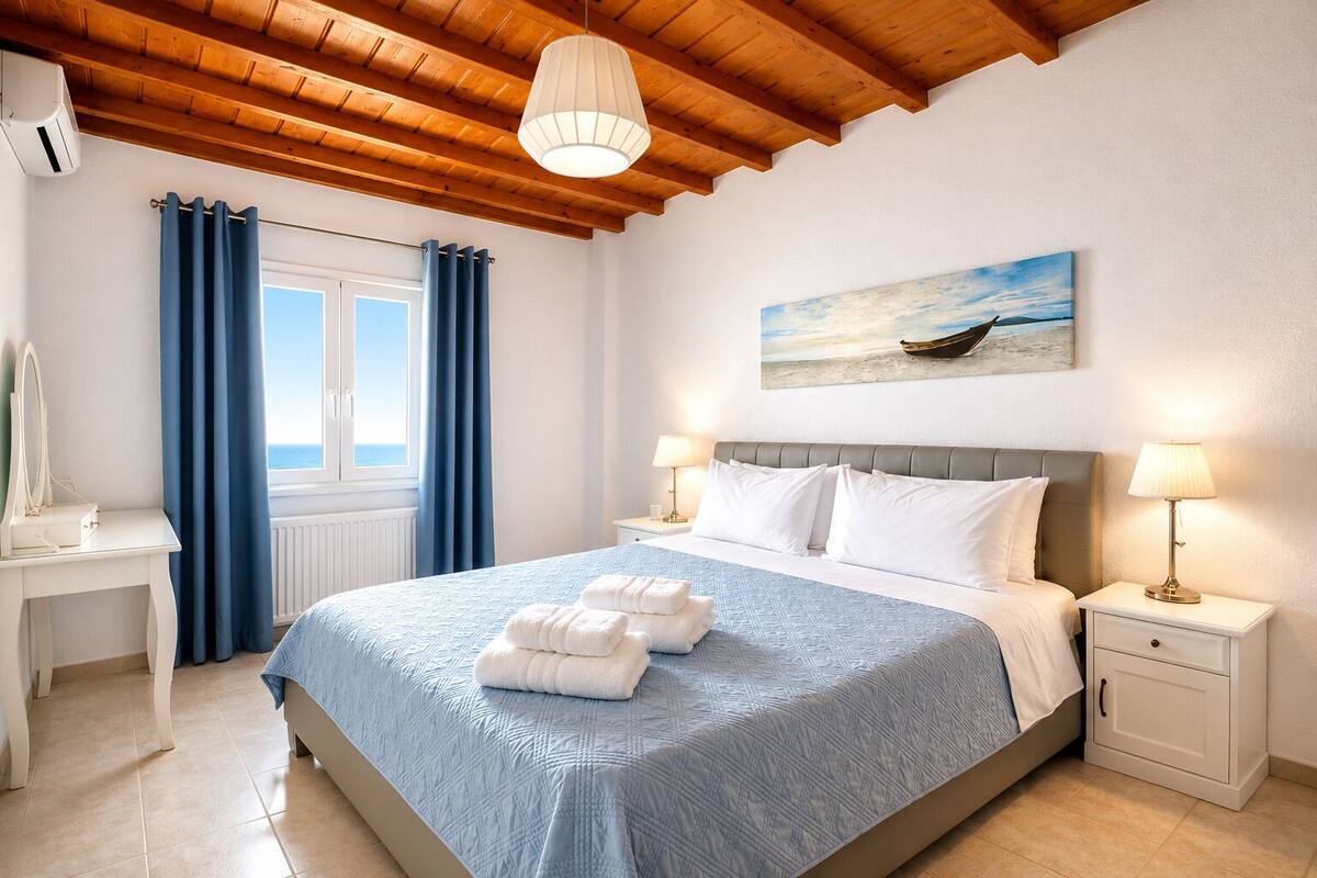 A bedroom with a bed, two bedside tables, a window with curtains, a painting, and a ceiling with wooden beams.