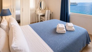 A bedroom with a bed, a desk with a mirror, a wardrobe, and a view of the sea. - Villa Oceania (Mykonos)