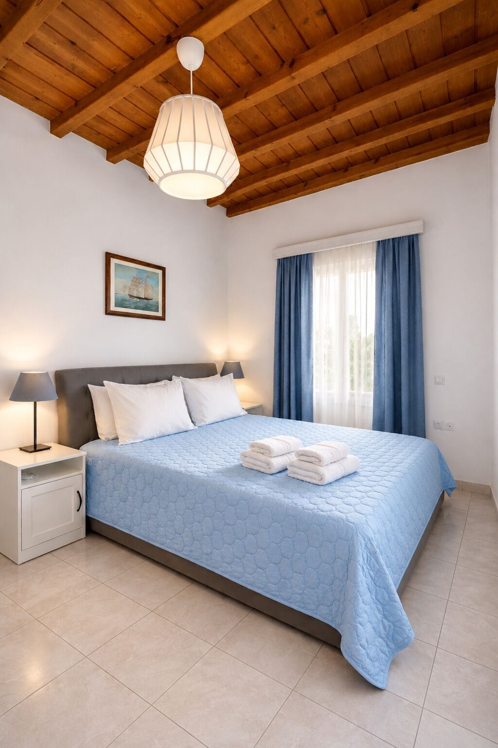 A bedroom with a bed, nightstands, a hanging light fixture, a painting, and a window with curtains.