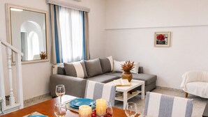 A modern living room with a sofa, a dining table set with blue plates and candles, a vase with dried flowers, and a framed picture on the wall. - Villa Oceania (Mykonos)