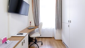 A modern room with a flat-screen TV mounted on the wall, a wooden desk with a chair, a radiator, and a wardrobe. - Riess City Rooms - Self Check-In (Vienna)