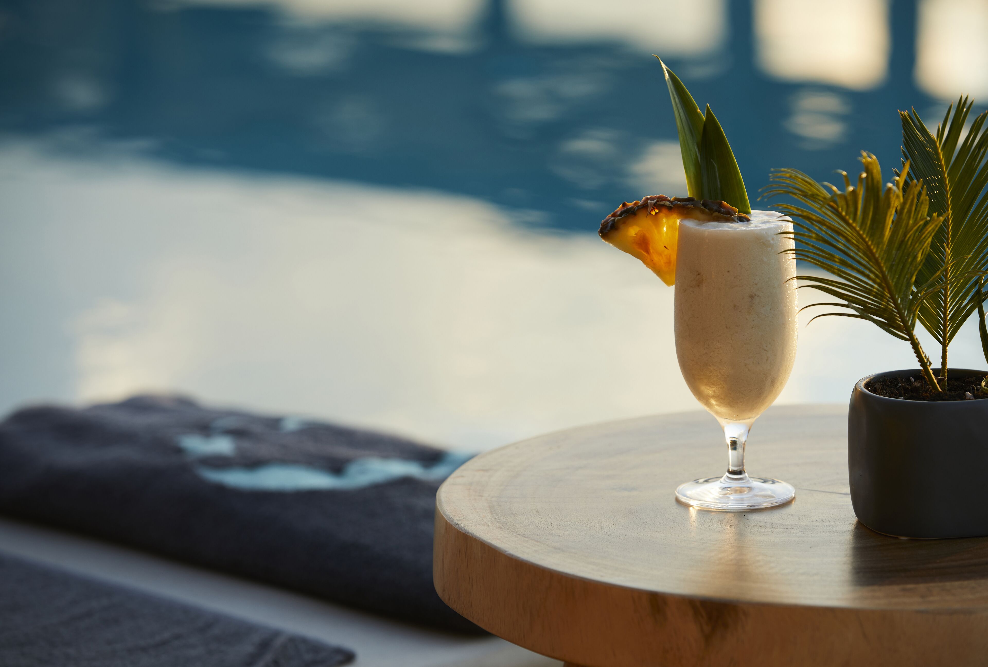 Een cocktailglas met garnering op een houten tafel bij een zwembad.