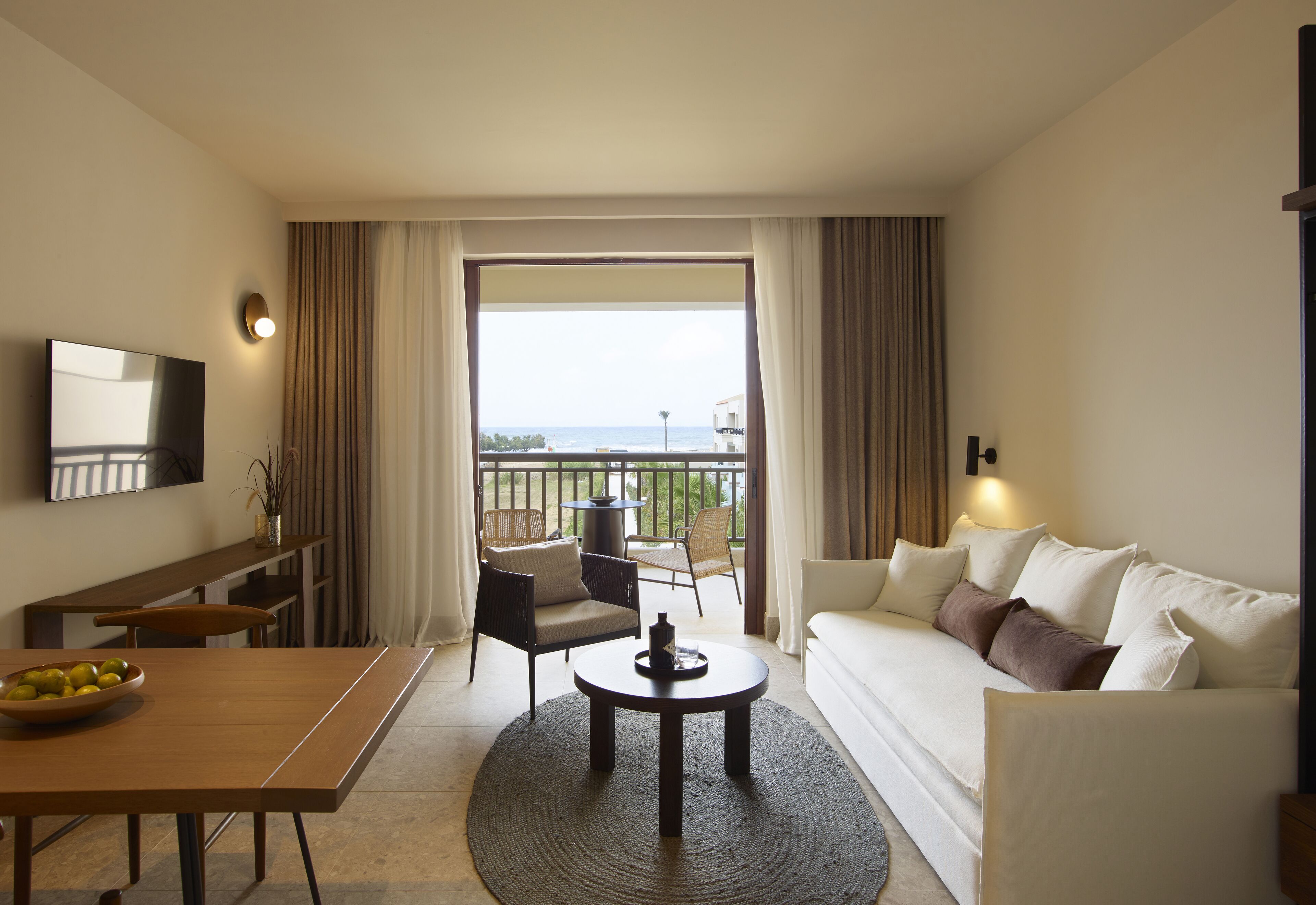 Een hotelkamer met balkon, een bank, een eettafel en een televisie.