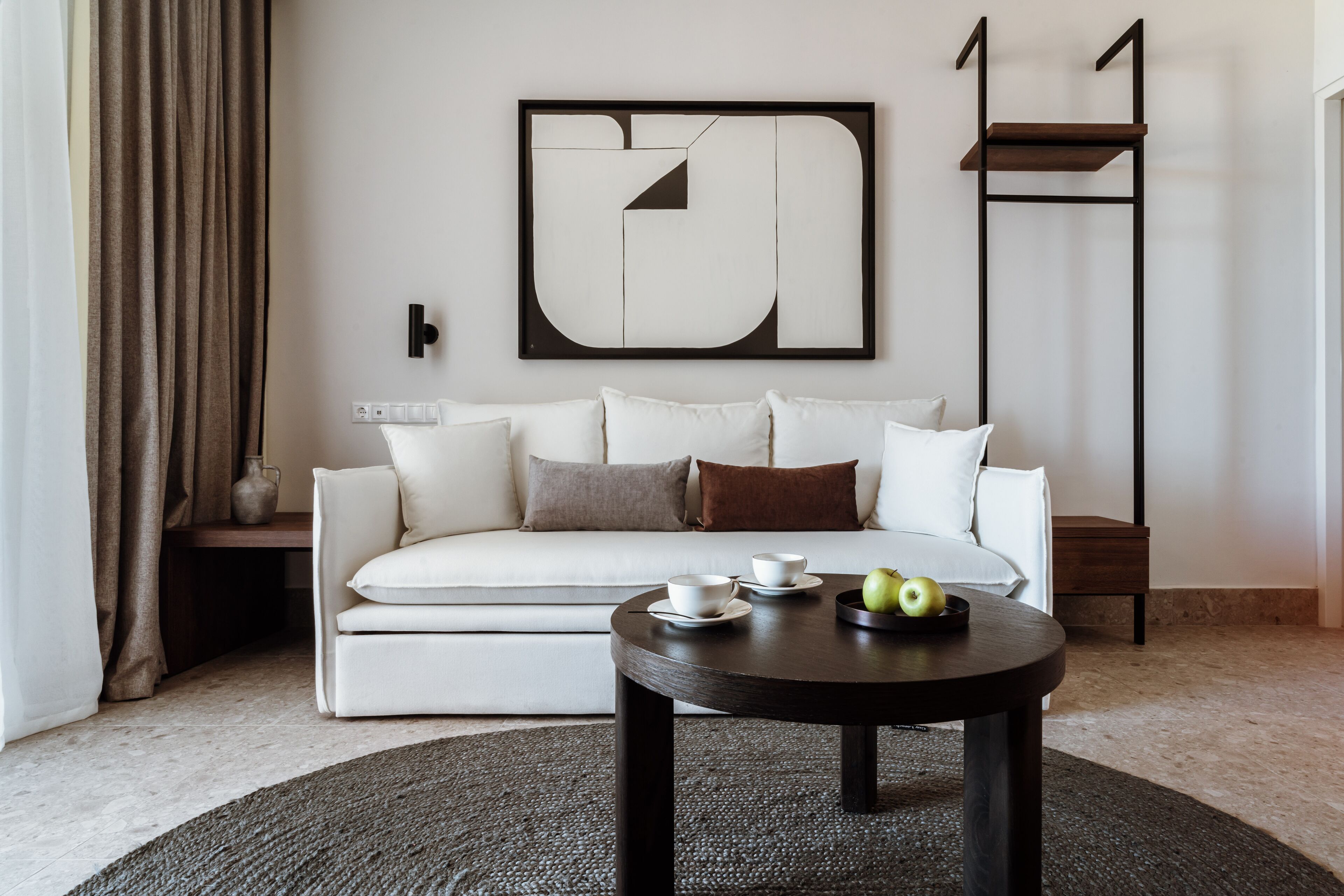A modern living room with a white sofa, a coffee table with apples, and a large abstract painting on the wall.