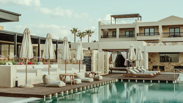 A pool area with lounge chairs, umbrellas, and a modern building with balconies. - Asterion Suites & Spa - Designed for Adults (Platanias)