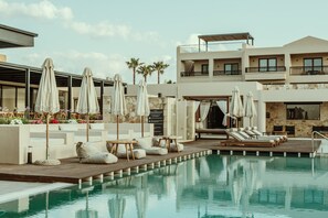 A pool area with lounge chairs, umbrellas, and a modern building with balconies.