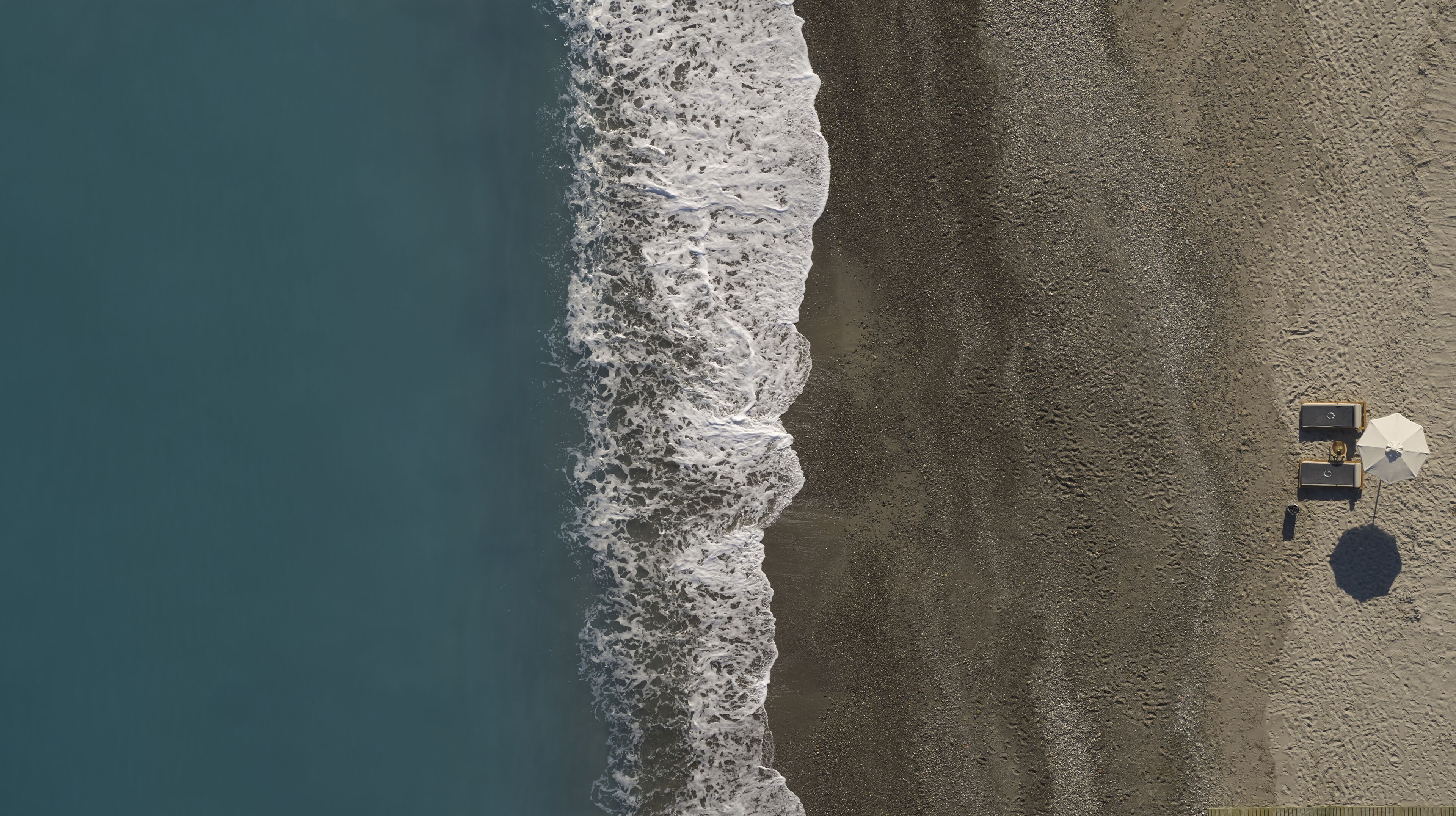 An aerial view of a beach with two sun loungers and an umbrella.