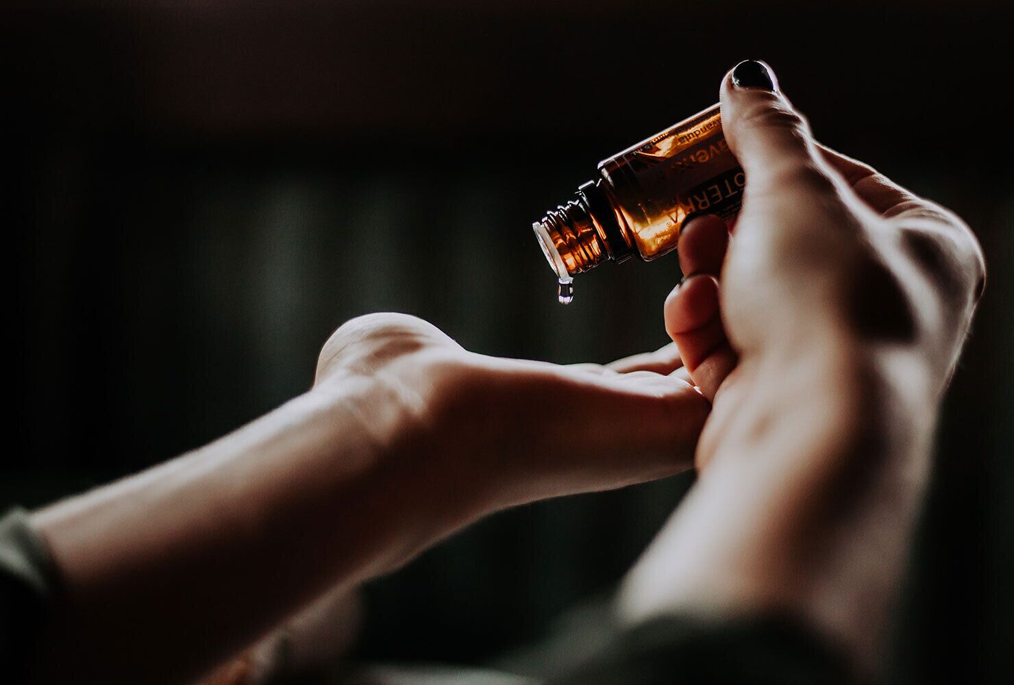 A hand holding a bottle with a drop of liquid at the end.