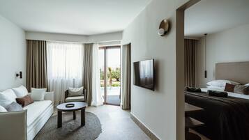 Una habitación de hotel moderna con sofá, una mesita redonda, cama con cabecera y televisión en la pared.