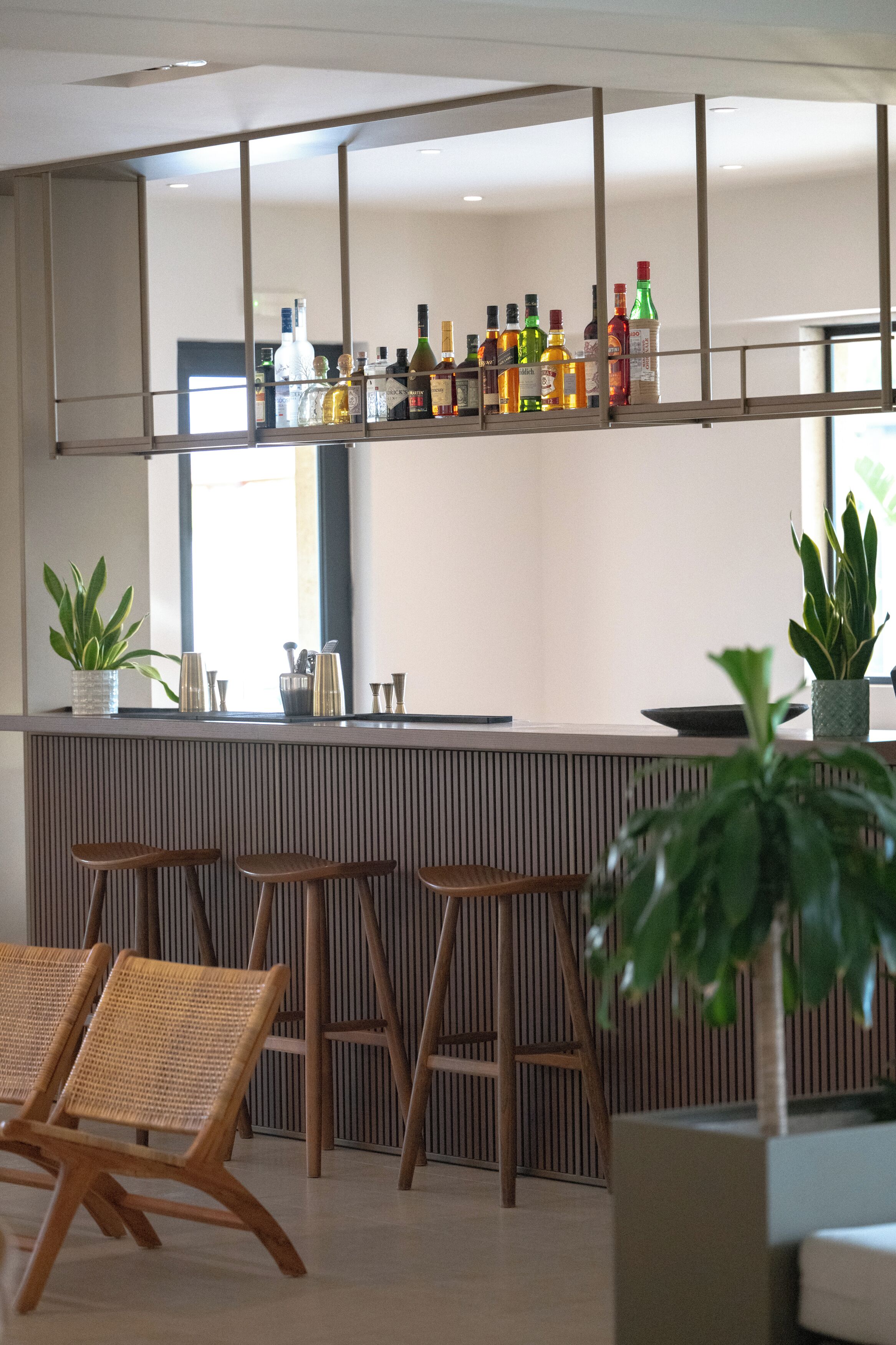 A modern bar area with a wooden counter, bar stools, and a variety of bottles.