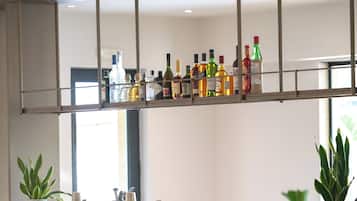 A modern bar area with a wooden counter, bar stools, and a variety of bottles.