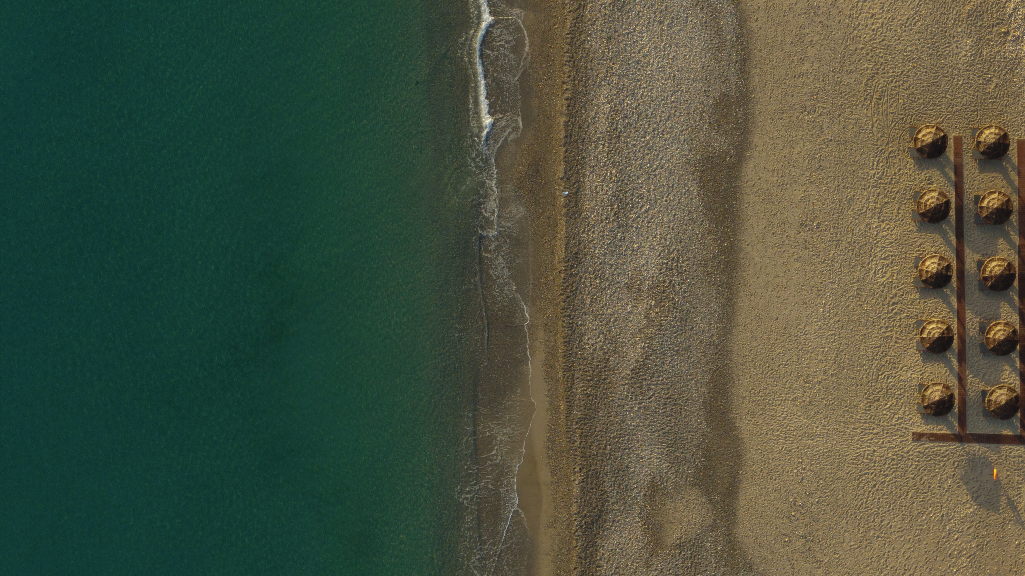 An aerial view of a beach with a row of sun loungers aligned parallel to the shoreline.