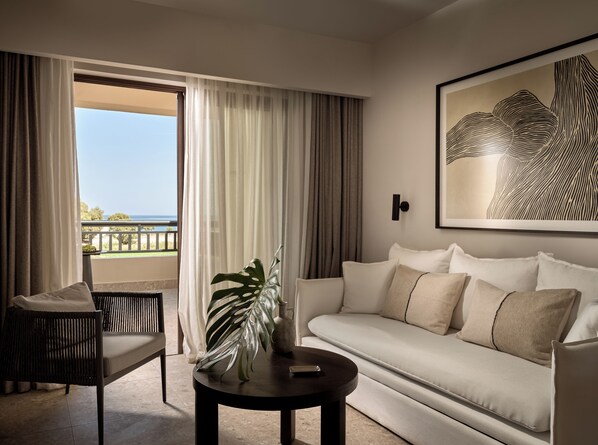 A modern living room with a sofa, a chair, a coffee table, and a view of the ocean through large windows. - Asterion Suites & Spa - Designed for Adults (Platanias)