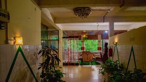 A hallway with tiled walls, potted plants, a chandelier, and a chair near a window. - Gahahe Hills Hotel (Bujumbura)