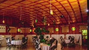 A dining area with round tables and chairs, a tiled floor, and a high ceiling with exposed beams. - Gahahe Hills Hotel (Bujumbura)