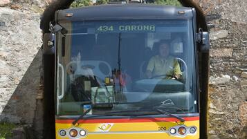 Ein gelber Bus mit der Nummer 434 und dem Zielort 'CARONA' fährt durch ein steinernes Tor.