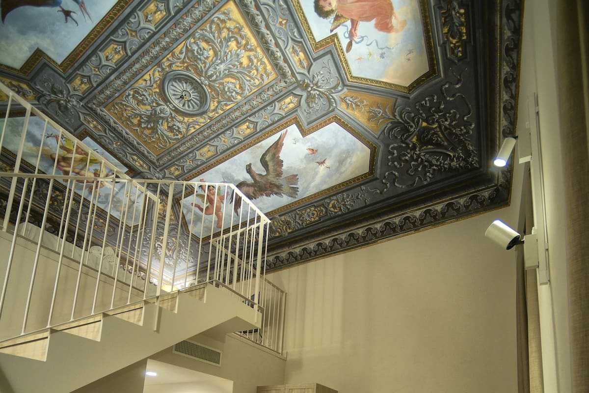 Un interior de diversos nivells amb una escala, un sofà i un sostre amb una obra d'art complexa.