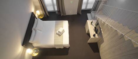 A hotel room with a bed, a desk with a bottle and glass, a chair, and a staircase.