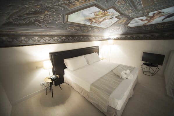 A hotel room with a large bed, two bedside lamps, a flat-screen TV, and a ceiling with intricate artwork.
