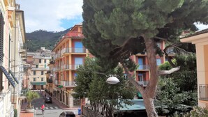 A street with multi-story buildings, balconies, and a large tree in the foreground. - Hotel Palazzo Vannoni (Levanto)