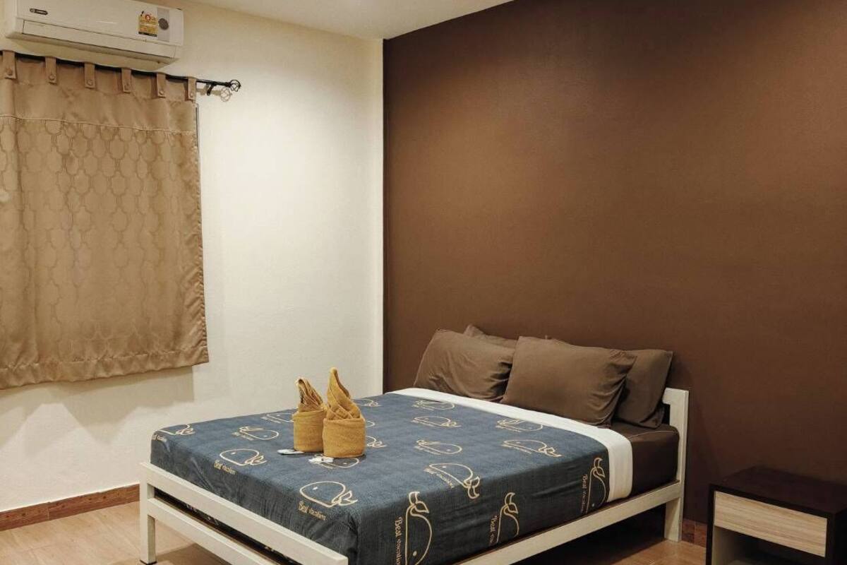 A bedroom with a bed, a nightstand, a blue rug, and a window with a curtain.