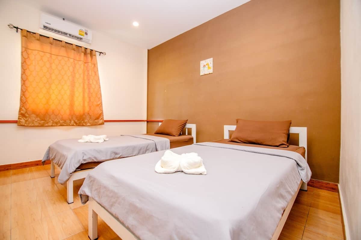 A hotel room with two single beds, a window with an orange curtain, a wall-mounted air conditioner, and a small artwork on the wall.