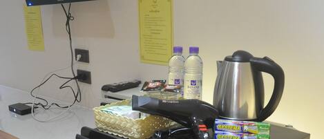 A kitchenette with a refrigerator, a coffee maker, and a TV displaying a nature scene.