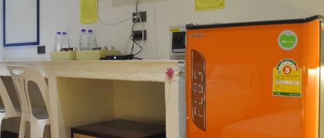 A room with a desk, a television mounted on the wall, and an orange refrigerator.