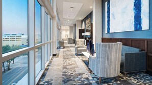 A hotel lobby with a long corridor, large windows, a patterned carpet, and a seating area with upholstered chairs.
