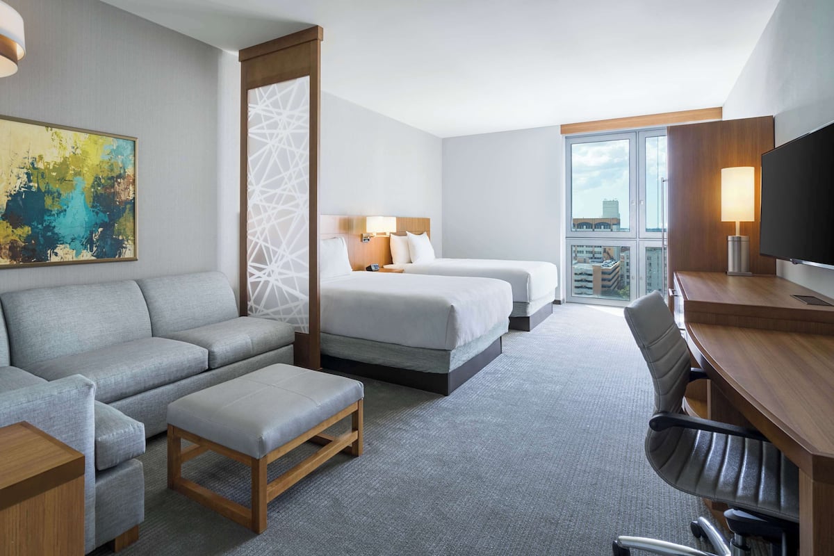 A hotel room with a sofa, two beds, a desk, and a TV.