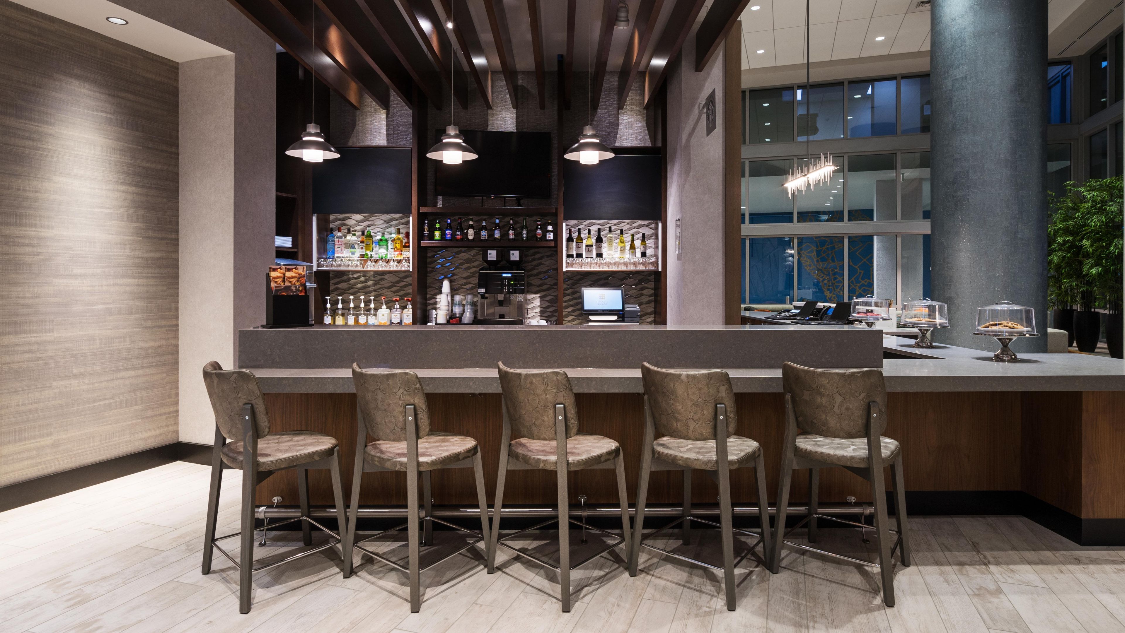 A bar area with a long counter, multiple bar stools, and a variety of bottles and glasses.